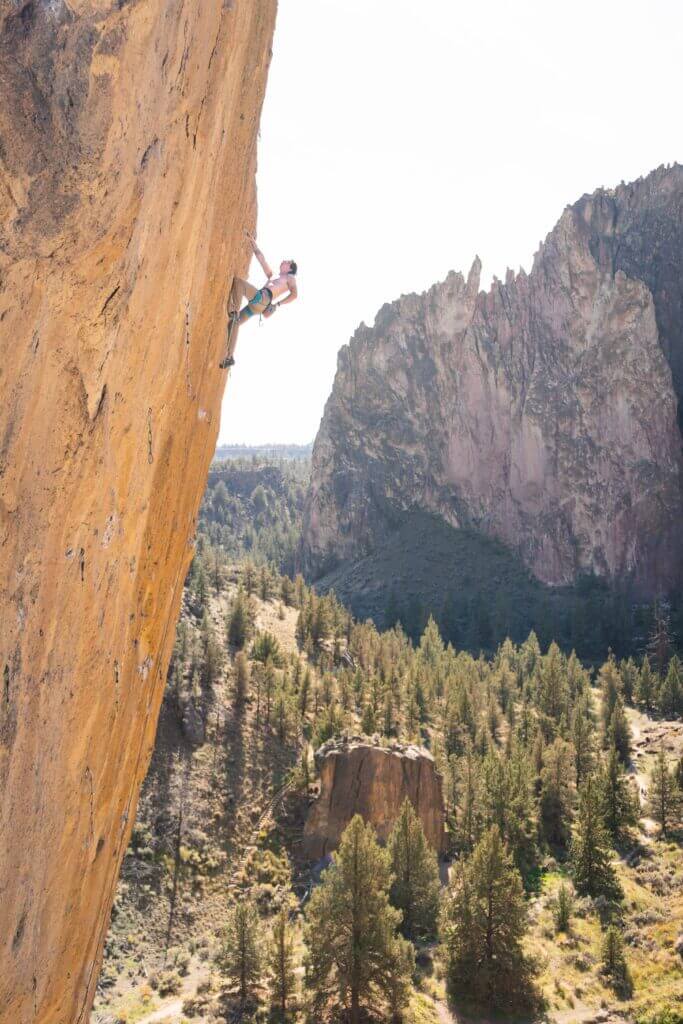 A sport climber chalks chalks his their hands and rests during a steep rock climb