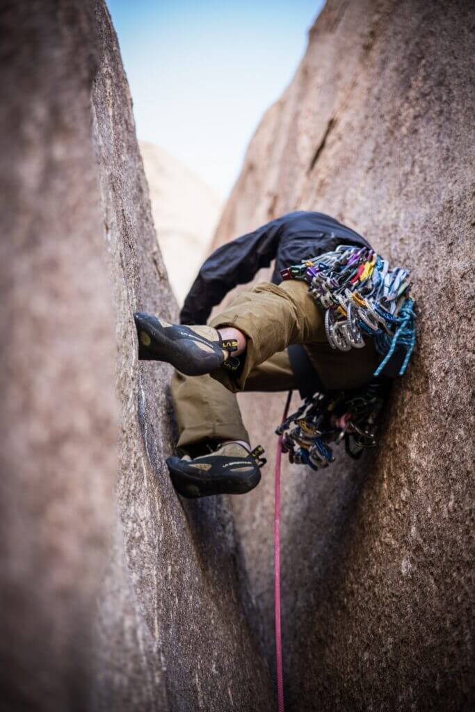 A trad climber with trad gear climbs upwards through a wide chimney system 